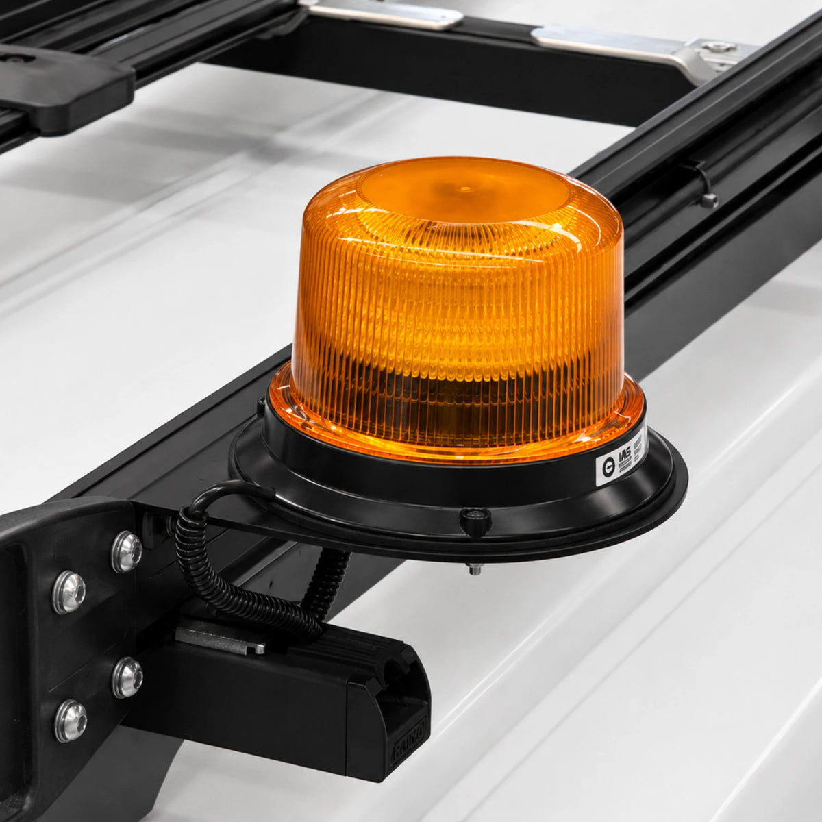An amber beacon mounted on a vehicle roof on a black metal roof rack bracket against a white vehicle roof.
