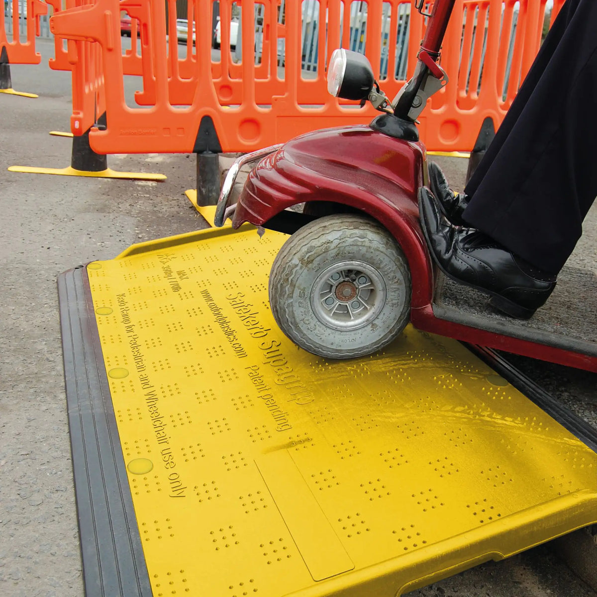 Mobility scooter being driven onto the SupaGrip SafeKerb ramp from the road, with orange pedestrian barriers behind