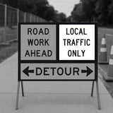 Road work ahead sign with detour instructions on a sidewalk.