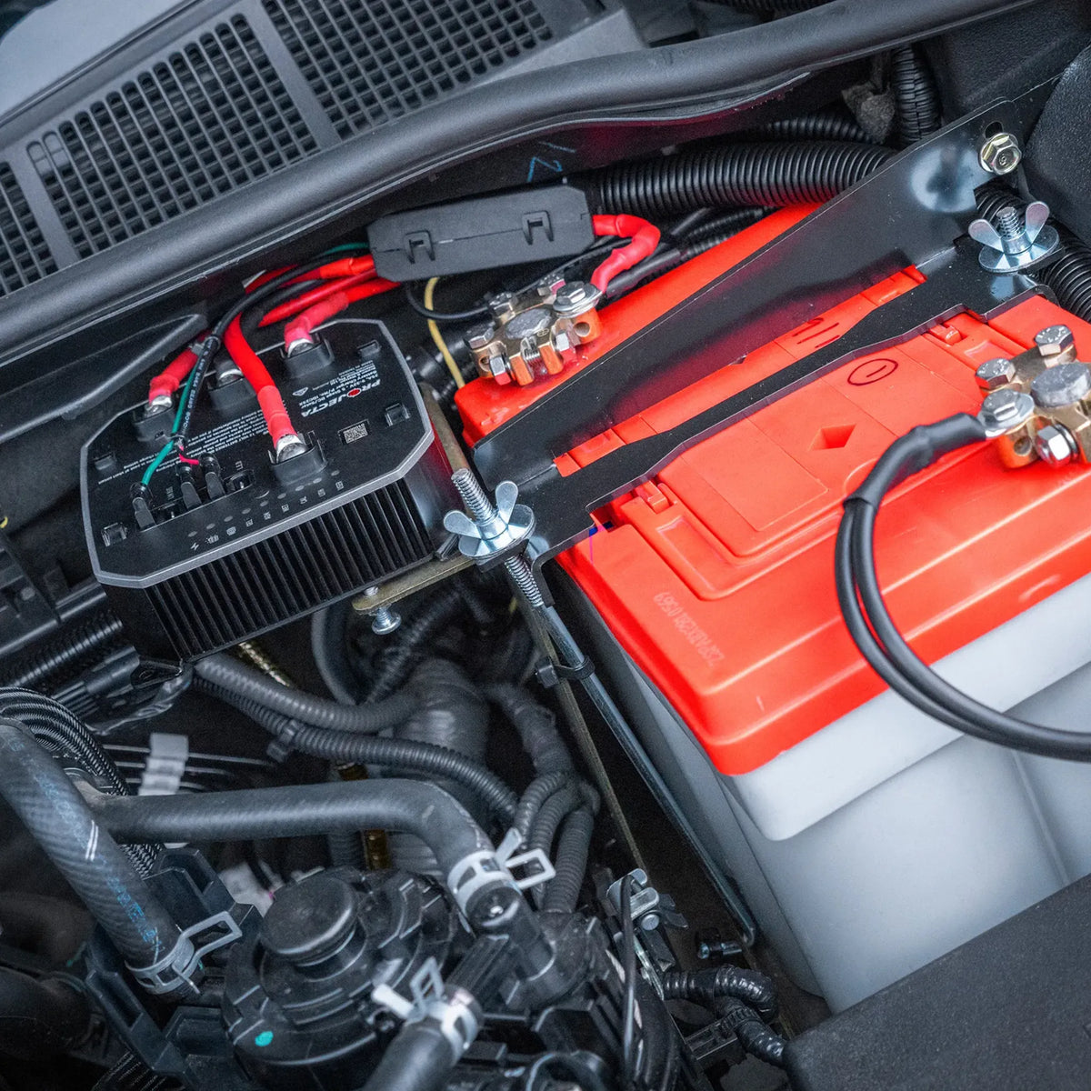 Close-up of a car's battery and electrical system with visible IDC25X connections under bonnet.
