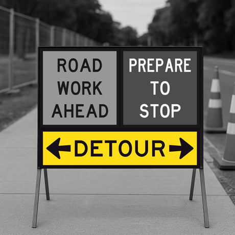 Temporary traffic control road work ahead sign with detour instructions on a stand.