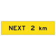 “NEXT 2 km” TM1-28B black text on retroreflective yellow – 1200x300mm corflute sign panel.