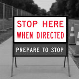 Road sign instructing drivers to stop when directed with traffic cones in the background.