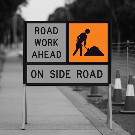 Road work ahead sign on a sidewalk with traffic cones in the background