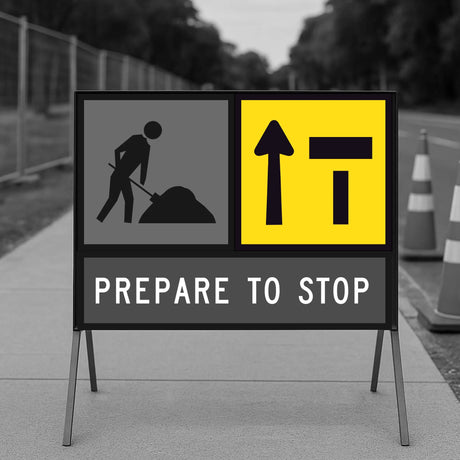 Construction warning sign with a figure shoveling and arrows indicating stop, on a road with traffic cones.