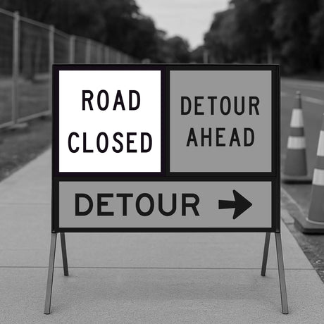 Temporary traffic control road closed and detour ahead signs on a stand with traffic cones in the background.