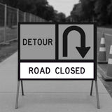 Road Closed and Detour sign panels mounted on a temporary sign frame on a footpath with fencing and traffic cones in the background
