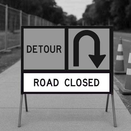 Road Closed and Detour sign panels mounted on a temporary sign frame on a footpath with fencing and traffic cones in the background