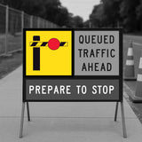 Road sign with boom barrier warning of queued traffic ahead with traffic cones in the background