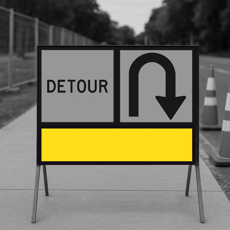 Temporary traffic control detour sign with a U-turn symbol and yellow blank on a road construction site.