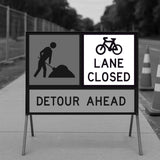 Road construction sign indicating 'Bicycle Lane Closed, Detour Ahead' and workman sign