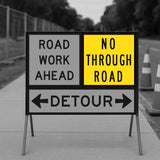 Temporary traffic control road work ahead sign with detour instructions on a road.