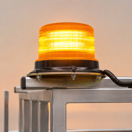 A bright orange emergency beacon light with a ribbed translucent dome and black base, mounted on a metal frame against a soft beige background.