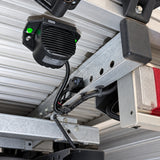 Brigade SA-BBS-97 reverse alarm installed upside down under the rear of a work vehicle tray, bolted to a galvanised steel crossmember beside the tail light, with the lead run in black corrugated conduit