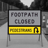 Pedestrians U-Turn corflute panel in the lower slot of a multi-message sign frame below a FOOTPATH CLOSED panel, on a footpath with traffic cones and temporary fencing