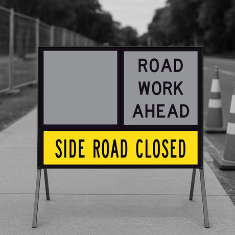 Side Road Closed TM1-32B 1200x300mm corflute panel in the lower slot of a multi-message sign frame below a blank yellow panel and a ROAD WORK AHEAD panel, on a footpath with traffic cones and temporary fencing