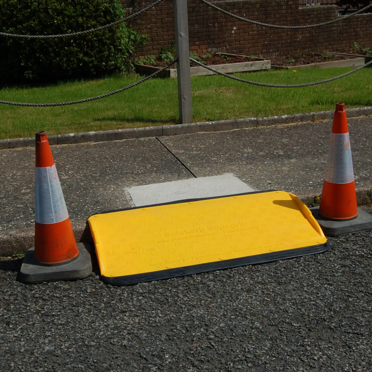 SupaGrip SafeKerb ramp in place against a kerb with a traffic cone either side, giving pedestrian access between footpath and road