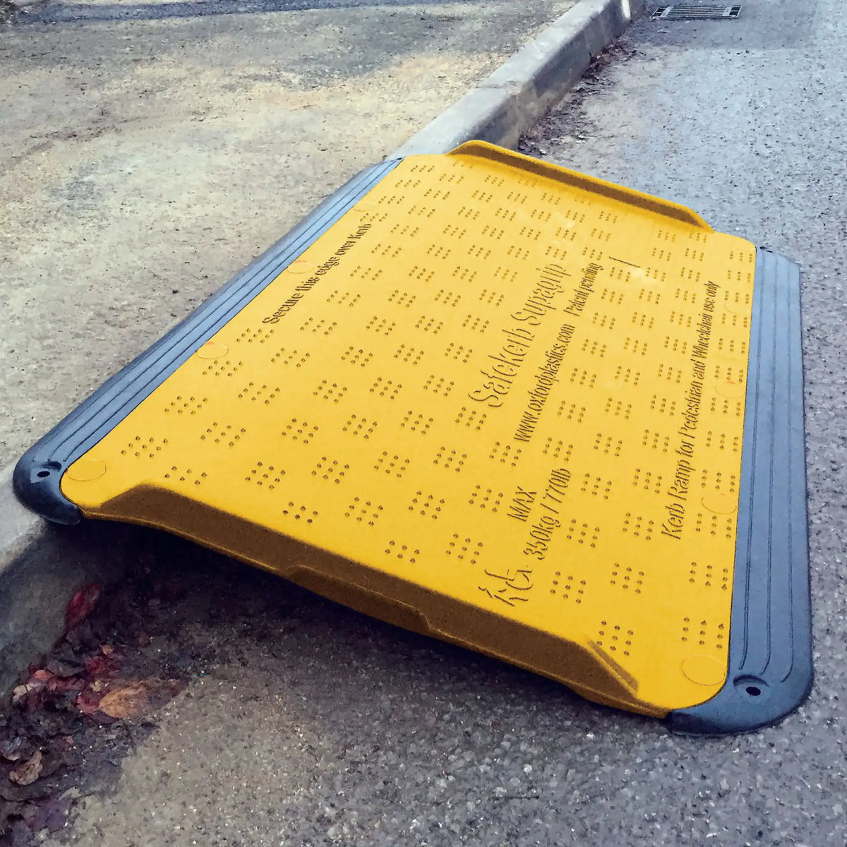SupaGrip SafeKerb ramp positioned over a kerb seen from the road, showing the moulded surface text and ribbed LowPro edges