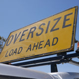 Close-up of the Oversize Load Ahead sign raised on a vehicle roof rack against a blue sky
