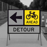 Bicycle Ahead sign panel mounted on a temporary sign frame with a Detour arrow panel and traffic cones in the background