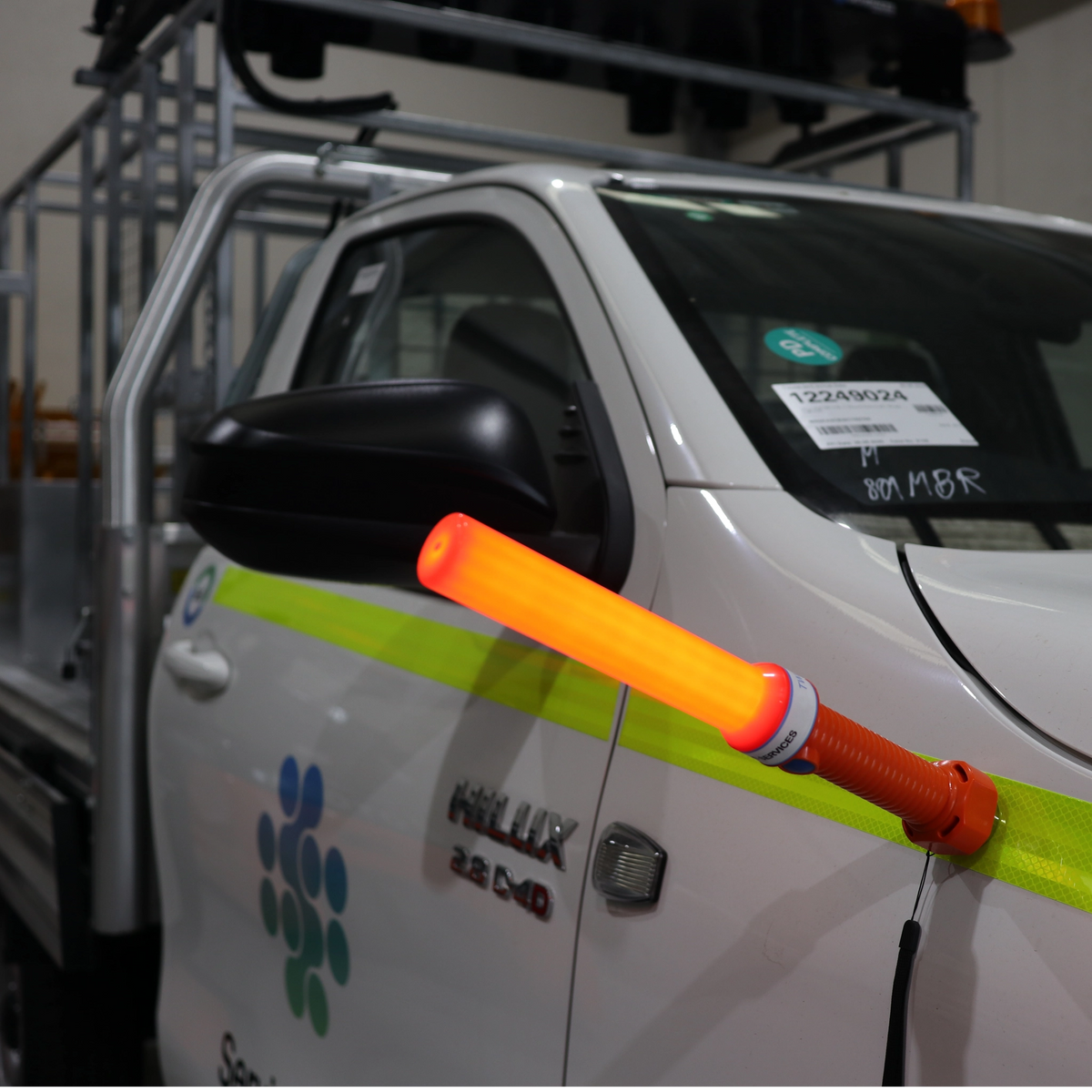 Lit orange LED marshalling wand held up against the door of a white Toyota Hilux ute in a workshop